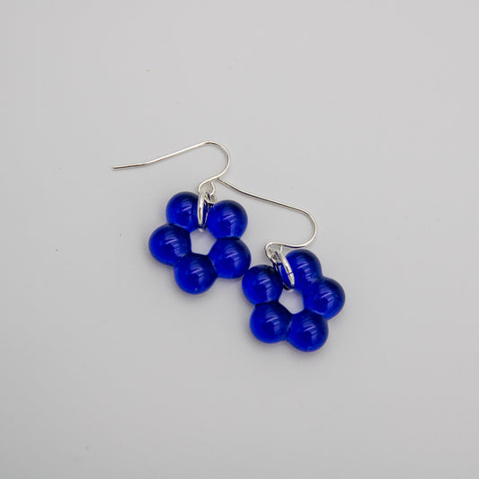 A pair of dangle earrings featuring five translucent cobalt blue beads arranged in a flower-like cluster, suspended from silver fishhook wires, shown on a neutral light gray background.