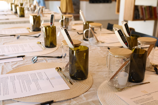 Table setting with green upcycled wine bottle candle vessels, papers, and utensils in a casual dining environment.