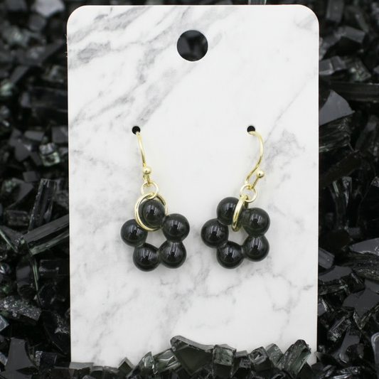 Black flower-shaped earrings on a marble card with a black stone background