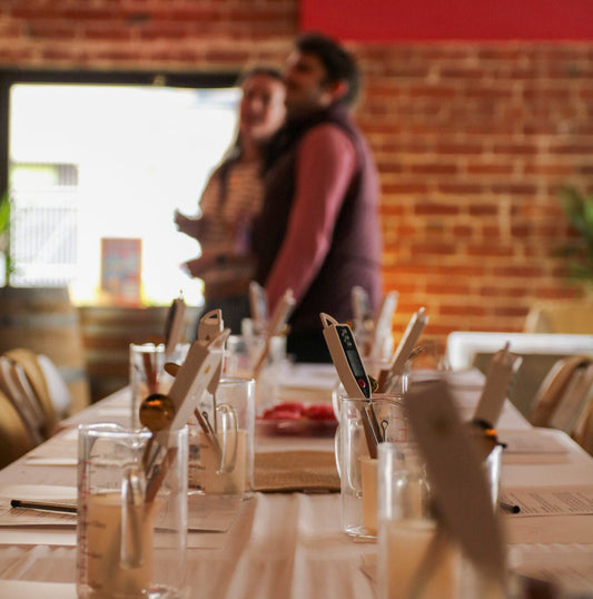 Communal table with candle making materials and a blurred couple in the background.