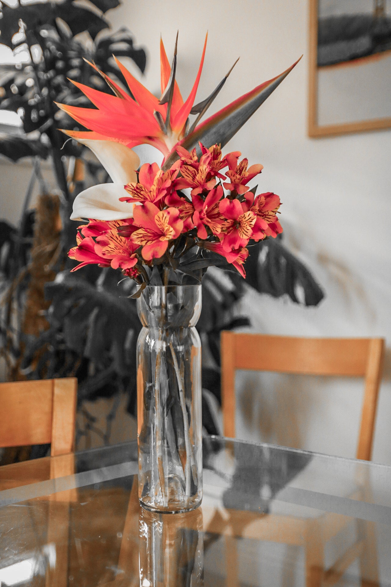 Clear vase with red and orange flowers on a glass table
