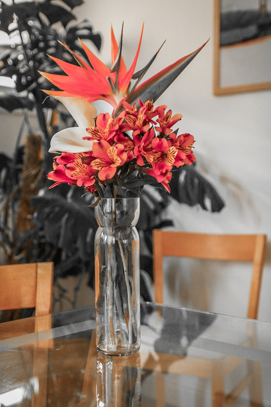 Clear vase with red and orange flowers on a glass table