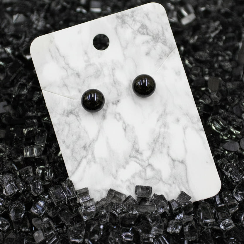 Tinted black glass gemstone earrings on a marble card with a tinted black glass textured background