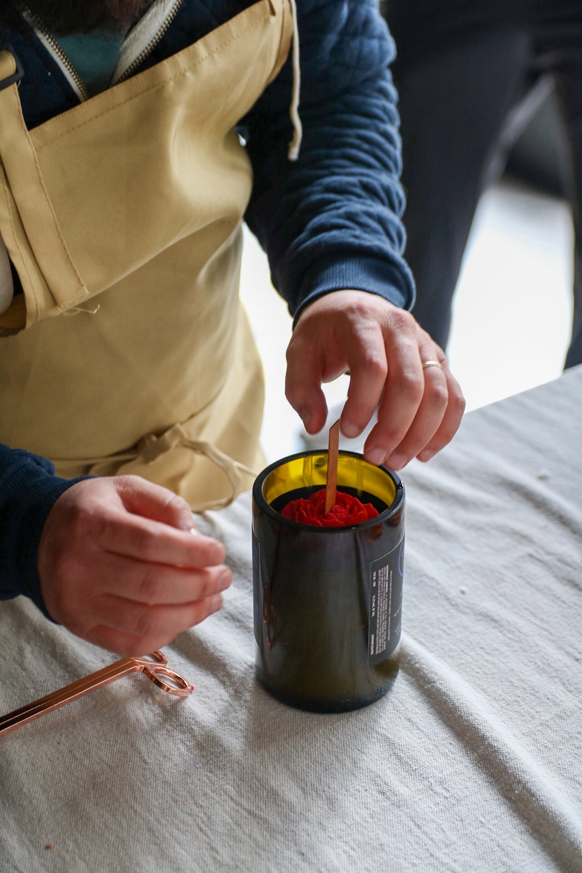 An upcycled wine bottle with a candle with a red flower on top 