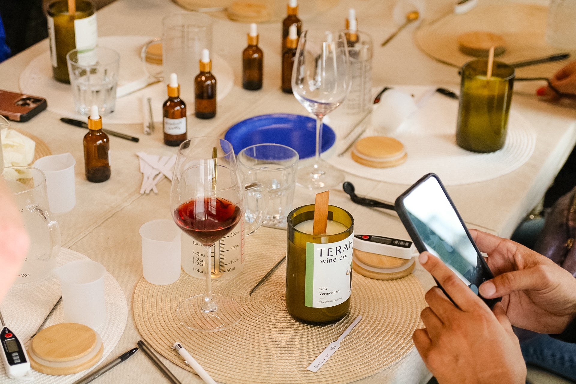 Table setting with wine glasses, bottles, and a candle with a person using a phone.