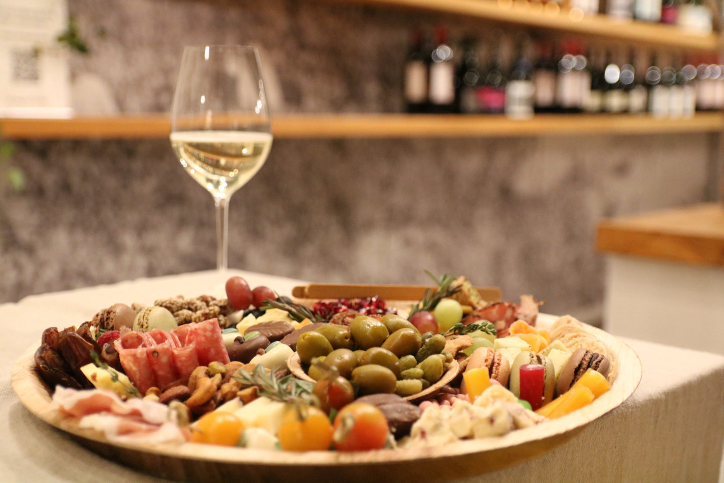 Platter of assorted meats, cheeses, and fruits with a glass of white wine on a wooden table.